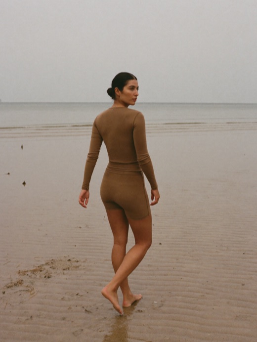 A woman walks along wet sand in a nutmeg long-sleeve top and matching shorts.