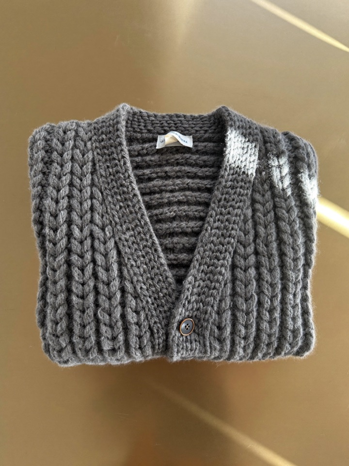 The Halle cardigan laid flat, showing the hand-framed stitch and horn buttons.